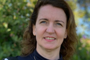 Sick young woman wearing protective mask during video call with mature doctor. Back view of patient with surgical face mask talking during conference call with her physician while staying at home in quarantine. Girl in online consultation with general practitioner on digital tablet.